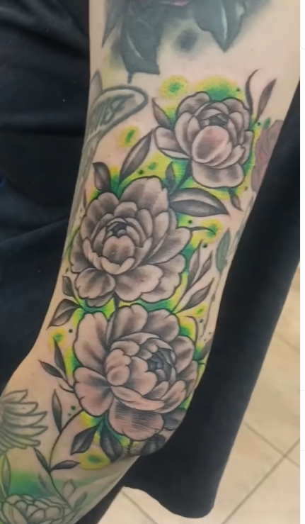 Black and grey floral sleeve tattoo with green and yellow color wash background